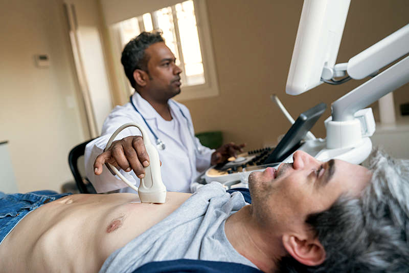 Doctor doing a heart ultrasound to a man-patient. 