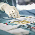 Cropped image of female surgeon reaching for syringes on table. Close-up of healthcare worker's hand wearing surgical glove. She is in emergency room.