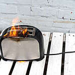 Black and steel toaster with two slices of toast catches fire.