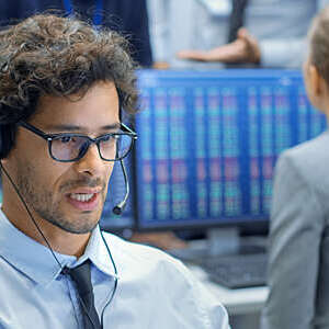Face shot of a stock trader with headset making a sale in a busy stock exchange office.