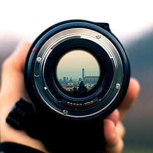 Close-up of camera objective with city view reflected in the lens.