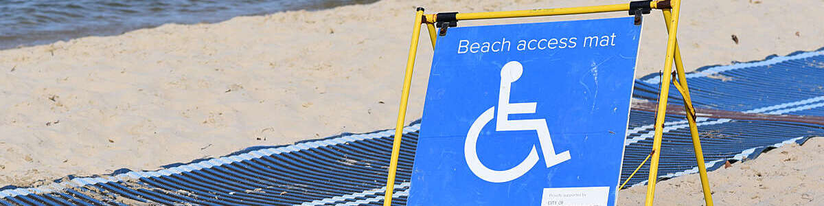 Big blue sign indicating wheelchair access to the beach via a mat rolled out on the sand.